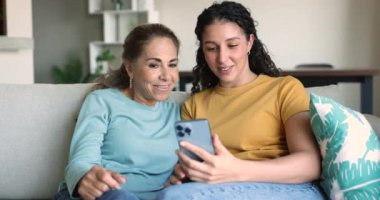 Genç 25 'lik kız, olgun 55' lik annelere yeni mobil uygulamalar gösteriyor. Kanepeye oturmuş cep telefonu ekranına bakıyor, komik videolar izliyor, internette aile eğlencelerinin tadını çıkarıyor. Modern teknoloji, yeni uygulamalar.