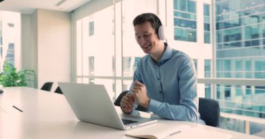 Millennial Man yöneticisi laptoptaki uygulamayı kullanarak kulaklık takıyor, web kamerası sohbeti yoluyla müşteriyle uzaktan iletişim kuruyor. Destek servisleri, görüşmeler çevrimiçi. Modern teknoloji kullanımı