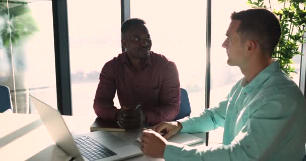两个千年一次的多族裔同事带头坐在工作场所的办公桌前进行对话 非洲商人聆听欧洲销售经理 银行顾问提供信息 谈论投资 — 图库视频影像
