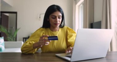 Çekici Hintli kadın kartla ödeme yapıyor, internetten alışveriş yapıyor, sipariş veriyor, mal ve e-hizmetleri satın alıyor, gülümsüyor, modern teknoloji kullanarak rahat ve rahat elektronik alışveriş yapıyor.