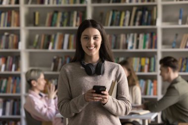 Cep telefonu tutan mutlu Latin öğrenci kız, kameraya dişlek gülümsemeyle bakıyor, daktilo çekiyor, iyi haberler alıyor, yüksek test sonuçları, sınav notları, eğitim sürecinin tadını çıkarıyor. Ön portre