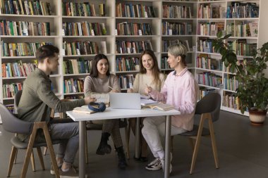 Üniversite kütüphanesinde okuyan, konuşan, gülen, ev ödevlerini tartışan, takım çalışmasının, eğitim sürecinin, açık kitap ve dizüstü bilgisayarın başında oturan çok ırklı üniversite öğrencilerinden oluşan mutlu bir ekip.