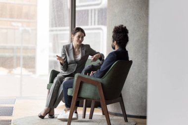 Modern ofisteki koltuklarda oturan iki çok uluslu iş arkadaşı, görüşlerini ve düşüncelerini paylaşıyor, ortak projeyi tartışıyor, diyalogla ilgilenen çözümleri paylaşıyor. İş, iletişim