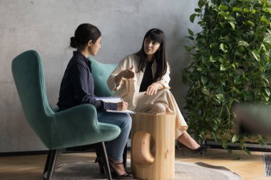 50 'lerin iş kadını stajyerlerle konuşuyor, koltuklarda oturuyor, tecrübeli akıl hocası çırağına profesyonel tavsiyeler veriyor, patron sekreter atamaları yapıyor, astı şefi dinliyor, görevler yazıyor.