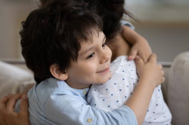 5 'li yaşlarındaki çocuk Hintli anneye sarılıyor, aile şefkatli bir anın tadını çıkarıyor, gülümsüyor sevimli bir çocuk ve şefkatli genç bir anne kucaklıyor, iyi bir ilişki ve güven, kanepede oturuyor, annelik kavramı.