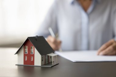 Emlakçı, emlakçı ve emlakçı masasındaki küçük aile evi modeli. Emlakçı kâğıt döküman yazıyor. Ev alıcısı anlaşma imzaladı. Kırpılmış atış