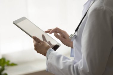 Tıbbi kayıtlar için dijital tablete başvuru yapan tıbbi pratisyen kadının görüntüsü, hastalarla internet bağlantısı. Üniformalı doktorun elinde. Yaklaş.