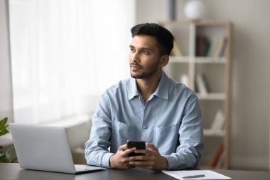 Düşünceli Hintli adam cep telefonunu tutuyor, masaya oturuyor, önemli e-postaları okuyor, iş teklifini düşünüyor, başka yöne bakıyor, sorunu çözmeyi düşünüyor ya da mesaj yoluyla mesaj atıyor, iş günü planlıyor, internette sohbet ediyor. E-servisler, uygulamalar