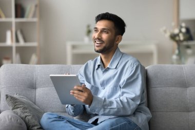 Gülümseyen Hintli adam elinde tablet, sosyal medyada sohbet ediyor, malları seçiyor, sipariş veriyor, pazar yeri başvurusu üzerinden alışveriş yapıyor, internetten alışveriş yapıyor, evde uzaktan iletişim kuruyor.