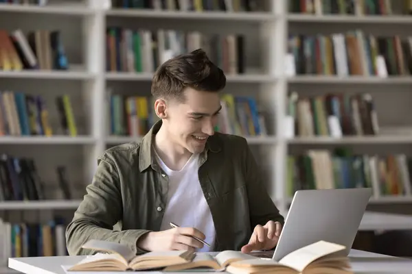 Stock image Happy student guy, teenage schoolboy prepare assignment, learn theory, studying in library using laptop. Generation Z gain new knowledge using modern wireless tech and internet resources. Education