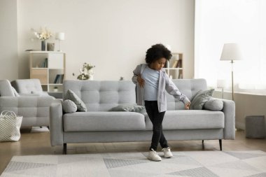 Güzel Afrikalı çocuk modern oturma odasında dans ediyor, şarkıya geçiyor, en sevilen pop sanatçısının hayranı dans ediyor, eğleniyor, eğleniyor, modern evde hobisinin tadını çıkarıyor, uzun metrajlı manzarası var.