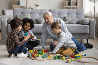 Çok nesilli aile modern evde ahşap demiryolu oynar. Büyük büyük baba üç çok ırklı çocukla demiryolu oynuyor, kardeşleri, tatlı torunları, birlikte oturma odasında vakit geçiriyorlar.