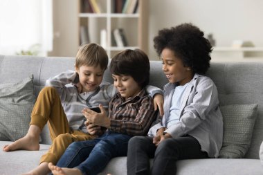 Oturma odasındaki kanepede oturan üç sevimli çocuk cep telefonlarıyla oyun oynuyorlar, akıllı telefondan komik videolar izliyorlar, arkadaşlar evde arkadaşlarıyla sohbet ederek vakit geçiriyorlar. Modern teknoloji
