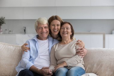 Neşeli genç yetişkin kız, yaşlı gri saçlı babaya sarılıyor ve olgun anne gülümsemesi kameraya bakıyor, evde aile fotoğrafı için poz veriyor. Çok nesilli insan bağları, sevgi ve anlayış