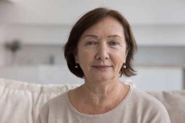 Kafadan yakından çekilmiş, olgun, güzel bir kadın. Evdeki rahat koltukta dinleniyor, kameraya bakıyor, poz veriyor. Kendinden emin ve huzurlu görünüyor. Orta yaş, yaşlılar için sağlık sigortası