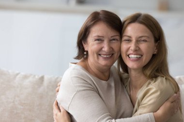 Genç ve yaşlı güzel kadınların portresi kameraya bak. Olgun bir anne, evdeki kanepede oturmuş milenyum kızına sarılıyor. Çok nesilli aile bağları, sevgi ve birlik
