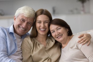 Güzel, sevgi dolu bir ailenin portresi, yakın görüş. Yetişkin 65 'lerin ebeveynleri milenyum çekiciliğine sarılıyorlar yetişkin 35' lerin kızları, kameraya poz veriyorlar koltukta oturuyorlar, aşkı hissediyorlar, birlikte paha biçilemez zaman geçiriyorlar.