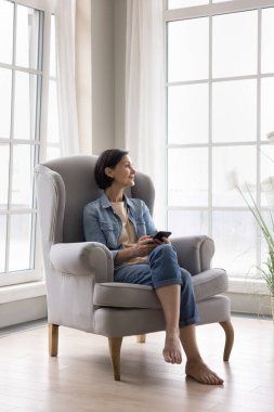 Orta yaşlı bir kadın oturma odasında modern akıllı telefonuyla dinleniyor, e-flört uygulaması kullanıyor, satın alınırken düşünüyor, internette sörf hakkında bilgi harcıyor ve boş zamanlarını internette geçiriyor. E-ticaret müşterisi, teknoloji