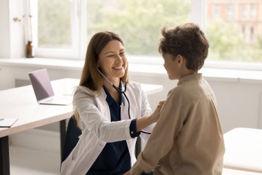Dost canlısı, çekici, doktor, steteskop tutan çocuk doktoru. Küçük çocuğun kalp atışlarını dinle. Gülümseyen genç uzman küçük şirin hastanın nefesini kontrol ediyor. Sağlık kontrolü, pediatri, sağlık hizmetleri.