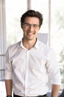 Dikey portre başarılı erkek ofis çalışanı, iş adamı eğitmeni veya akıl hocası iş yerinde poz verir, günlük beyaz gömlek giyer ve gözlük takar kameraya bakar, şirket pozisyonundan memnun olur, kariyer gelişimi sağlar.