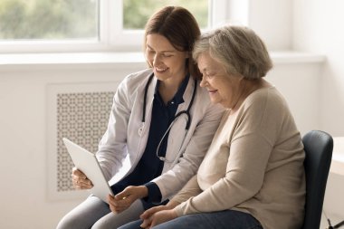 Üniformalı genç bayan doktor yaşlı kadına danışıyor dijital tablet kullanıyor, laboratuvar sonuçlarını ekranda gösteriyor, danışmanlık yapıyor, elektronik reçete yolluyor. Sağlık hizmetleri, modern teknoloji