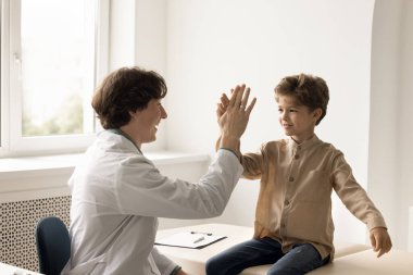 Üniformalı genç doktor klinikteki küçük hasta çocuğa beşlik çakıyor ve başarılı tedaviyi kutluyor. Neşeli çocuk doktorla görüşmeni bitir. Çocuk sağlık hizmetleri