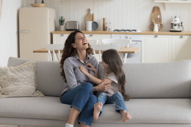 Neşeli anne ve kız kanepede oynuyorlar, birbirlerini gıdıklıyorlar, gülüyorlar, çığlık atıyorlar, eğleniyorlar. Anneye sarılma, anneliğin tadını çıkarma, ev eğlencesi, etkinlik.