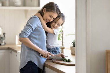 Genç bir kadın salata için salatalık keser, mutfakta sevgi dolu bir kızla vakit geçirir, şefkatli bir anneye sarılır, evde birlikte vakit geçirir. Aile hafta sonu, annelik, doğal yemek hazırlığı.