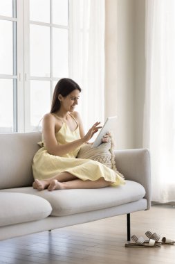 Güzel bir kadın rahat bir kanepede dijital tabletle dinleniyor, İnternet 'te sörf yapıyor, bir şeyler alıyor, kıyafetler elektronik ticari satış siteleri kullanıyor, evde e-alışverişin keyfini çıkarıyor. Piyasa uygulamaları