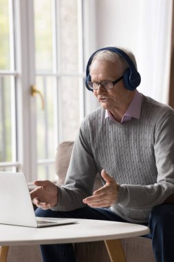 Ciddi, kablosuz kulaklık takan yaşlı bir adam internetteki terapistle sohbet ediyor. Video çağrı uygulaması üzerinden arkadaşlarıyla uzaktan iletişim kuruyor. Danışmanla konuşuyor.