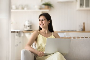 Gülümseyen çekici genç kadın evde dizüstü bilgisayarla kaygısız boş vakitlerin tadını çıkarıyor. Elektronik ticaret istemcisi, çevrimiçi iş, öğrenim ya da eğlence, uzaktan iletişim, blog, serbest internet kullanımı