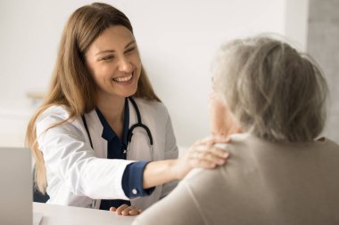 Beyaz üniformalı mutlu kadın doktor empati kuruyor ve yaşlı bir hastanın omzuna dokunuyor. Doktorla konuştum. İyileşme ve başarılı tedavi için tebrik ederim. Check-up, yaşlı bakımı