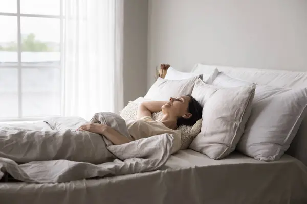 stock image Older woman sleeping alone in double bed in modern, light bedroom, looks serene while resting in early morning at home, enjoy comfortable orthopaedic mattress and fresh beddings, having healthy sleep