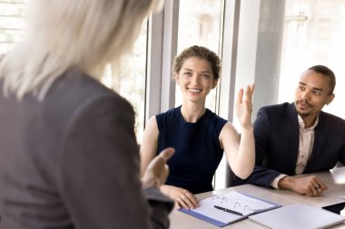 Genç iş kadını, kadın antrenör liderliğindeki konferans odasında düzenlenen kurumsal eğitim etkinliği sırasında soru soran meslektaşlarıyla birlikte masada oturuyor. İş semineri, eğitim, girişim, oy