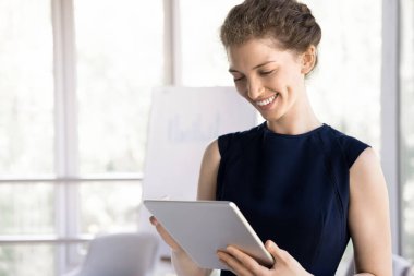 İş yerinde dijital masa kullanan çekici bir iş kadını. Milenyum ofis çalışanı elinde modern bir cihaz tutuyor, müşteriye e-posta ile mesaj gönderiyor, ortağına cevap gönderiyor, çevrimiçi sunum hazırlıyor.