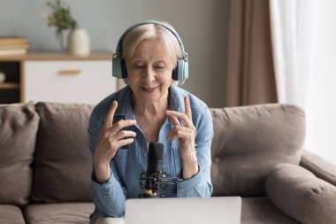 Yaşlı kadın blogcu kulaklık takıyor. Profesyonel mikrofon kurşunlu web sitesine konuşuyor ya da dizüstü bilgisayarla yayın yapıyor. Kıdemli radyo sunucusu, hoparlör programı yayında.