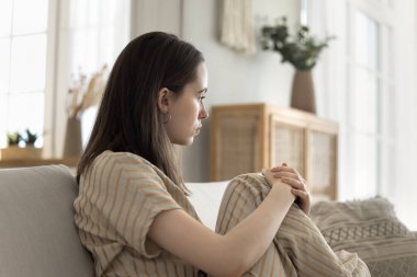 Üzgün, yalnız, genç bir kadın. Kanepede oturuyor, düşünceli görünüyor, depresyon geçiriyor, kişisel sorunları var, melankolik bir ruh hali içinde, ayrılığı düşünüyor, negatif duyguları, stresi, tükenmişliği.