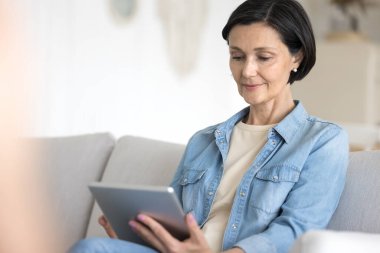 Dijital tablette çalışan olgun bir kadın rahat bir koltukta oturur, modern cihazlarla evde yalnız başına dinlenir, internetten ve e-servislerden mal satın alır, haftasonunu internet kullanımında kablosuz teknolojilerde geçirir.
