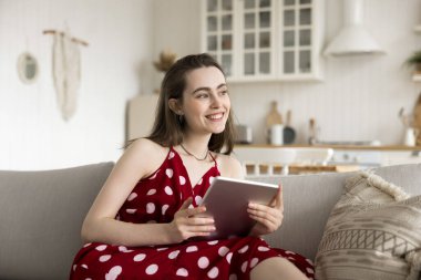Güzel, gülümseyen genç bir kadın modern dijital tablet cihazıyla evde vakit geçiriyor, elektronik ticaret hizmetlerinden keyif alıyor, çevrimiçi alışveriş yapıyor, sosyal ağlarda arkadaşlarıyla sohbet ediyor.