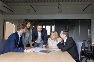 Ciddi takım arkadaşları, genç ve olgun çalışanlardan oluşan bir grup grafiklerde, çizelgelerde ve diyagramlarda gösterilen satış istatistiklerini gözden geçirir, evrak işleri yapar, planlama başlar, fikirleri paylaşır, takım çalışmasında yer alan projeyi geliştirir.