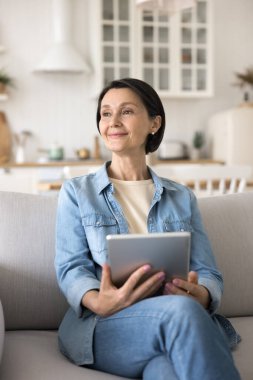 Evde dijital tabletle dinlenen rüya gibi olgun bir kadın. Emeklilik, mal satın alma, sipariş verme, elektronik ticari uygulama veya web sitelerinin müşterisi için modern kablosuz teknoloji kullanımı