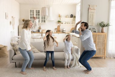 Çocukları olan mutlu çift oturma odasında favori müziğe taşınıyor, gülüyor, eğleniyor, yeni evde dans ediyor, sıcak zeminde yalınayak zıplıyor, küçük çocuklar genç ebeveynleriyle aktif hafta sonu tatilinin tadını çıkarıyor.