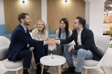 Bir grup mutlu iş ortağı, dört genç ve olgun iş arkadaşı, modern ofis koridorunda oturan takım arkadaşları el sıkışıyor. Arkadaşlık, ortaklık kurmak, ticari anlaşma yapmak, saygı göstermek.