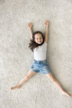 En güzel manzara, küçük anaokulu kızı sıcak zeminde uzanmış, kollarını açmış, bacaklarını açmış kameraya bakıp gülümsüyor, evde yalnız başına kaygısızca eğleniyor.