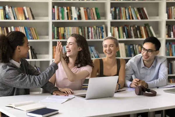 Mutlu öğrencilerin beşlik çakması iyi sonuçları kutluyor, hedefe ulaştıktan sonra heyecan ve memnuniyeti ifade ediyor, görevi tamamlıyor, dostça bir jest yapıyor, cesaretlendiriyor, yoldaşlık ve takım çalışması gösteriyor.