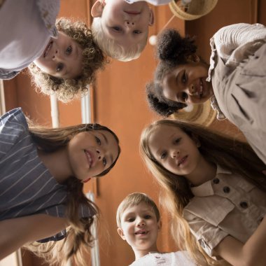 Yüzlerinizi kapatın. Mutlu, çok ırklı küçük kızlar ve çocuklar daire şeklinde sıralanmış gülümseyin. Kameraya bakın ve içeride eğlenceli vakit geçirin. Alfa kuşağı çocuklarının portresi, en iyi arkadaşlar, dostluk