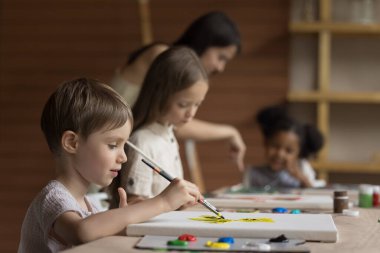 Grup sınıfında resim yapan güzel bir öğrenci, sanat okulunda küçük çocuklar için okuyor, tuvale resimler çiziyor, masaya oturuyor, boya fırçası tutuyor, paleti boyayla kullanıyor, yaratıcı kurslara katılıyor.