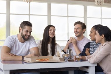 Çoklu etnik kızlar ve erkekler içeride takılıyor, masada oturmuş pizza ve içeceklerle konuşurken gülüyorlar, birlikte zaman geçiriyorlar mutlu oluyorlar. Hafta sonları arkadaşlık ve rahatlık.