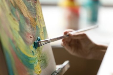 Kapalı görüşlü kadın ressam elinde boya fırçasıyla tuvale dokunuyor, kapalı alanda akrilik boya çiziyor. Sanatçı resim çiziyor, turkuaz vuruşlar uyguluyor, sanat eserleri üzerinde çalışıyor, yaratıcı süreçlerle meşgul.