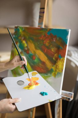 Kadın ressam resim yaratır, atölyede çalışmaya hazırlanır, bilinmeyen kadın sanatçıların ellerini paleti renkli boya ve boya fırçasıyla kaplar, tuvale resim çizer.